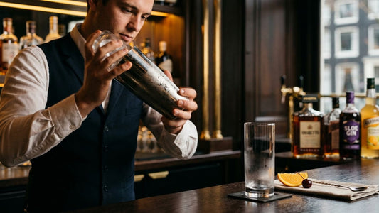Bartender pouring ingredients into a cocktail shaker to prepare an Alabama Slammer drink with vodka, gin, and sloe gin