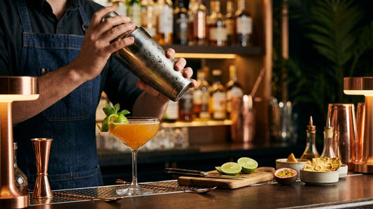Professional bartender pouring golden tropical cocktail into coupe glass with fresh mint garnish at upscale bar