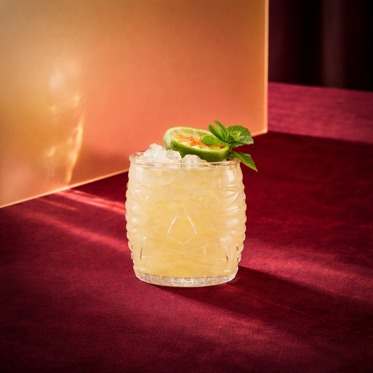 aged mai tai cocktail with dry orange liqueur and genever in a tiki glass with a lime wheel and a mint sprig on a red surface