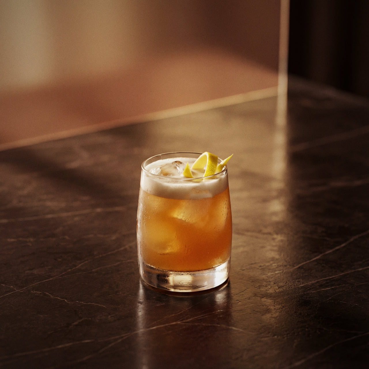 amaretto sour cocktail with amaretto liqueur in a rocks glass with a lemon twist on a dark surface