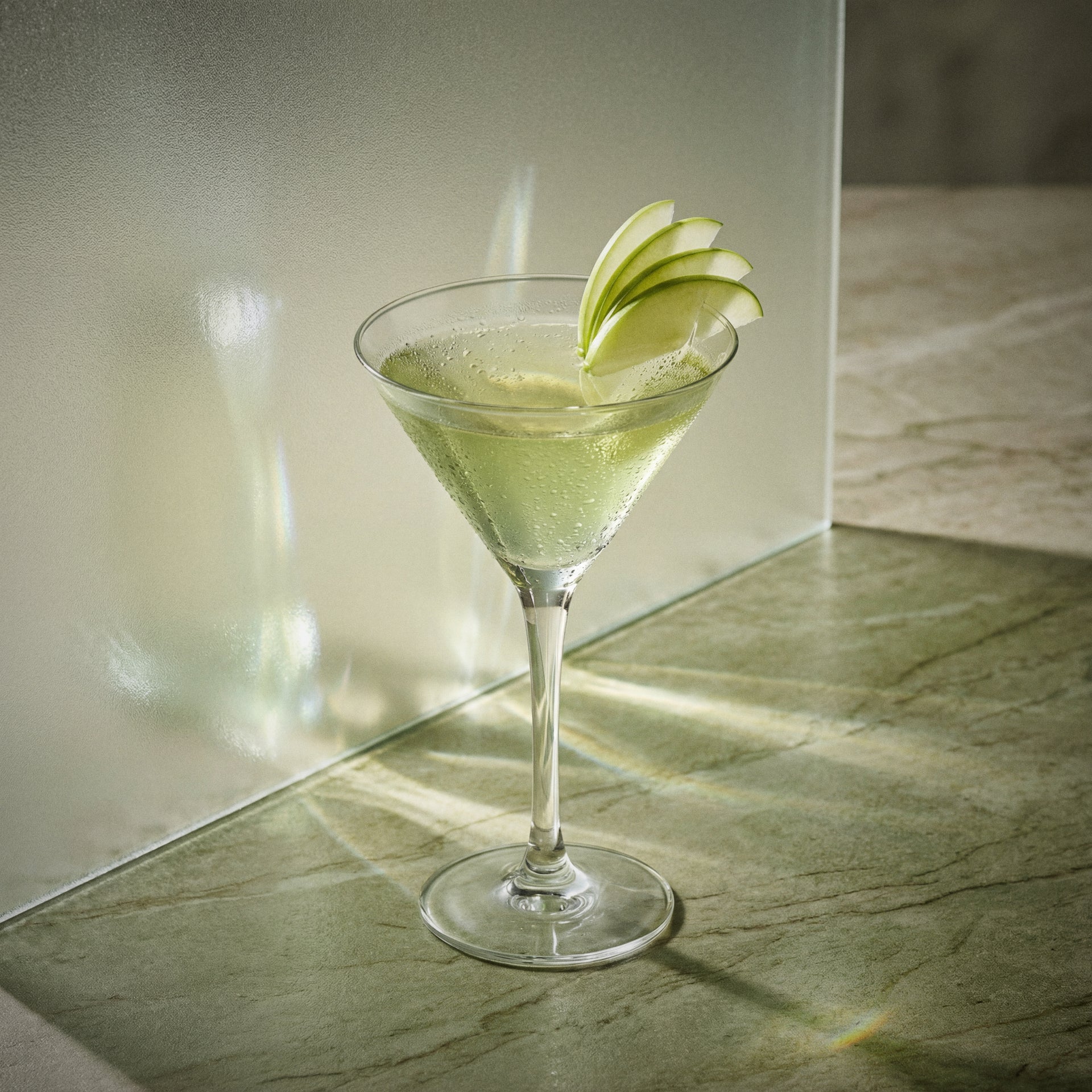appletini cocktail with sour apple liqueur and vodka in a martini glass with apple slices on a reflective surface