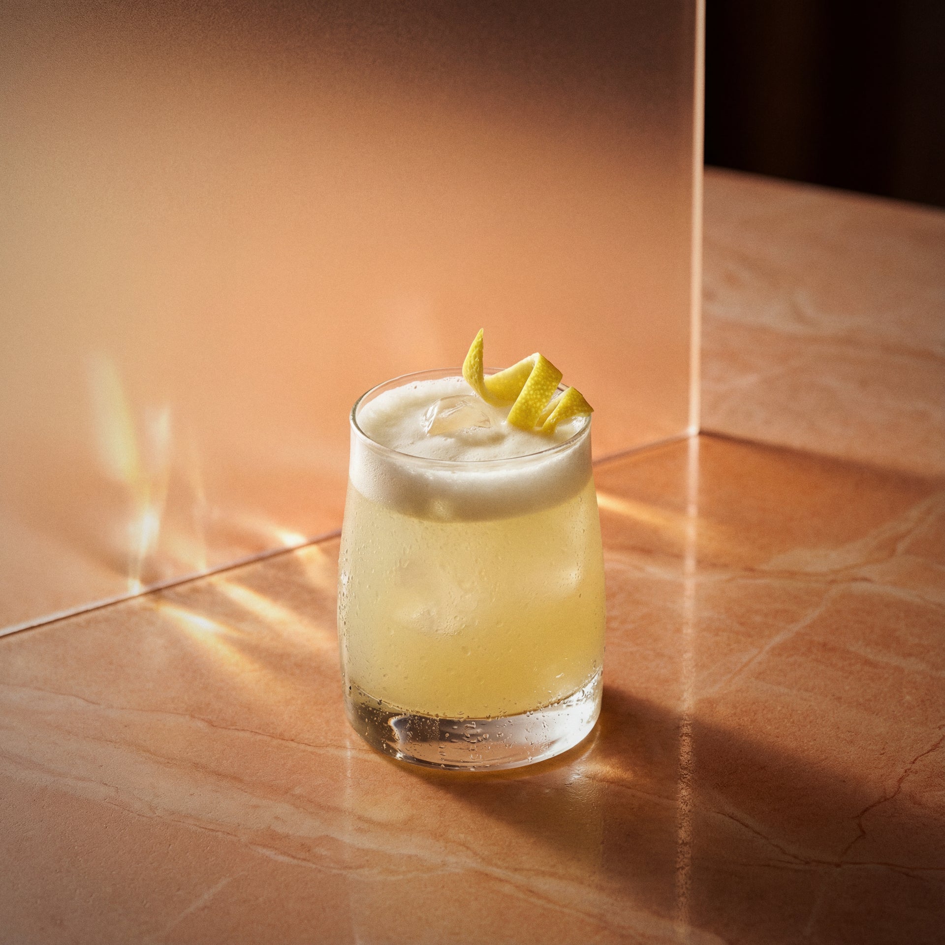 apricot brandy sour cocktail with apricot brandy liqueur in a rocks glass with a lemon twist on a textured background
