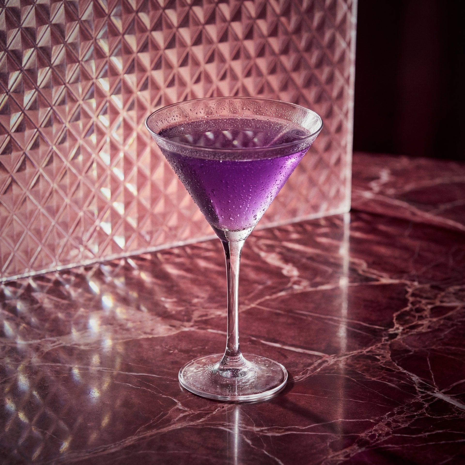 aviation cocktail in a martini glass on with maraschino liqueur and parfait amour liqueur a marble surface with a patterned wall in the background