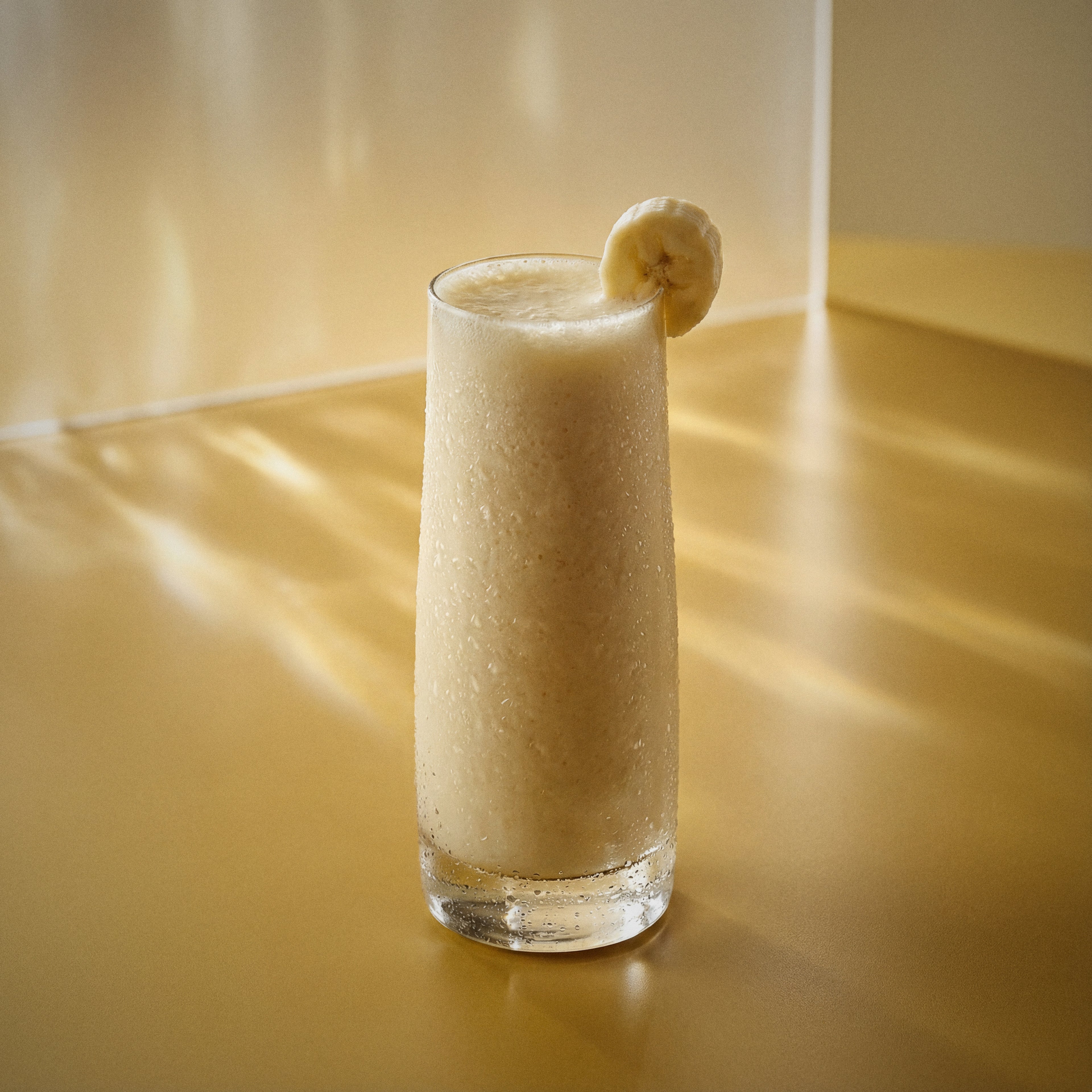 banana colada cocktail with coconut liqueur and banana liqueur in a highball glass with a slice of banana on a reflective surface
