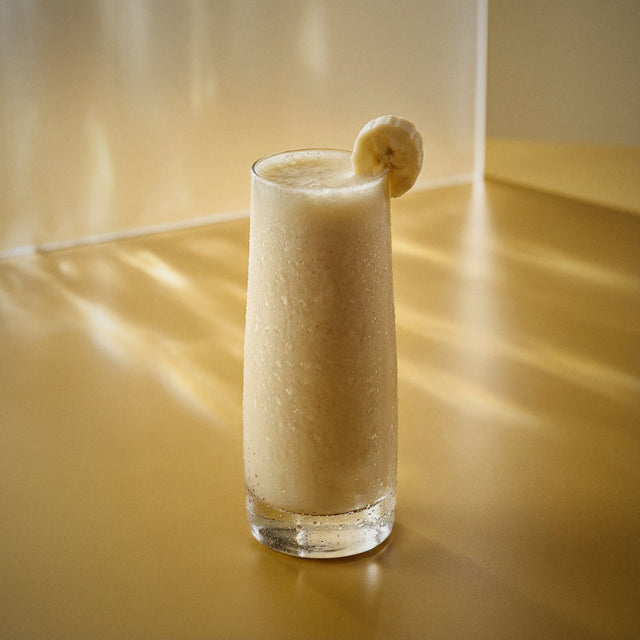 banana colada cocktail with coconut liqueur and banana liqueur in a highball glass with a slice of banana on a reflective surface
