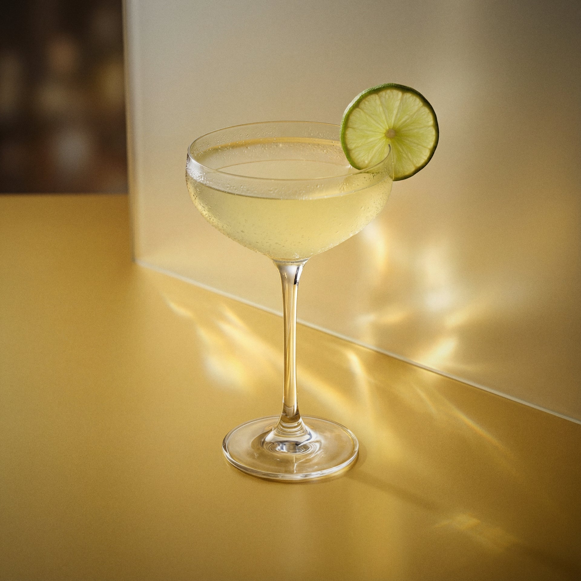 banana daiquiri cocktail in a coupe glass with a lime wheel with banana liqueur on a yellow surface
