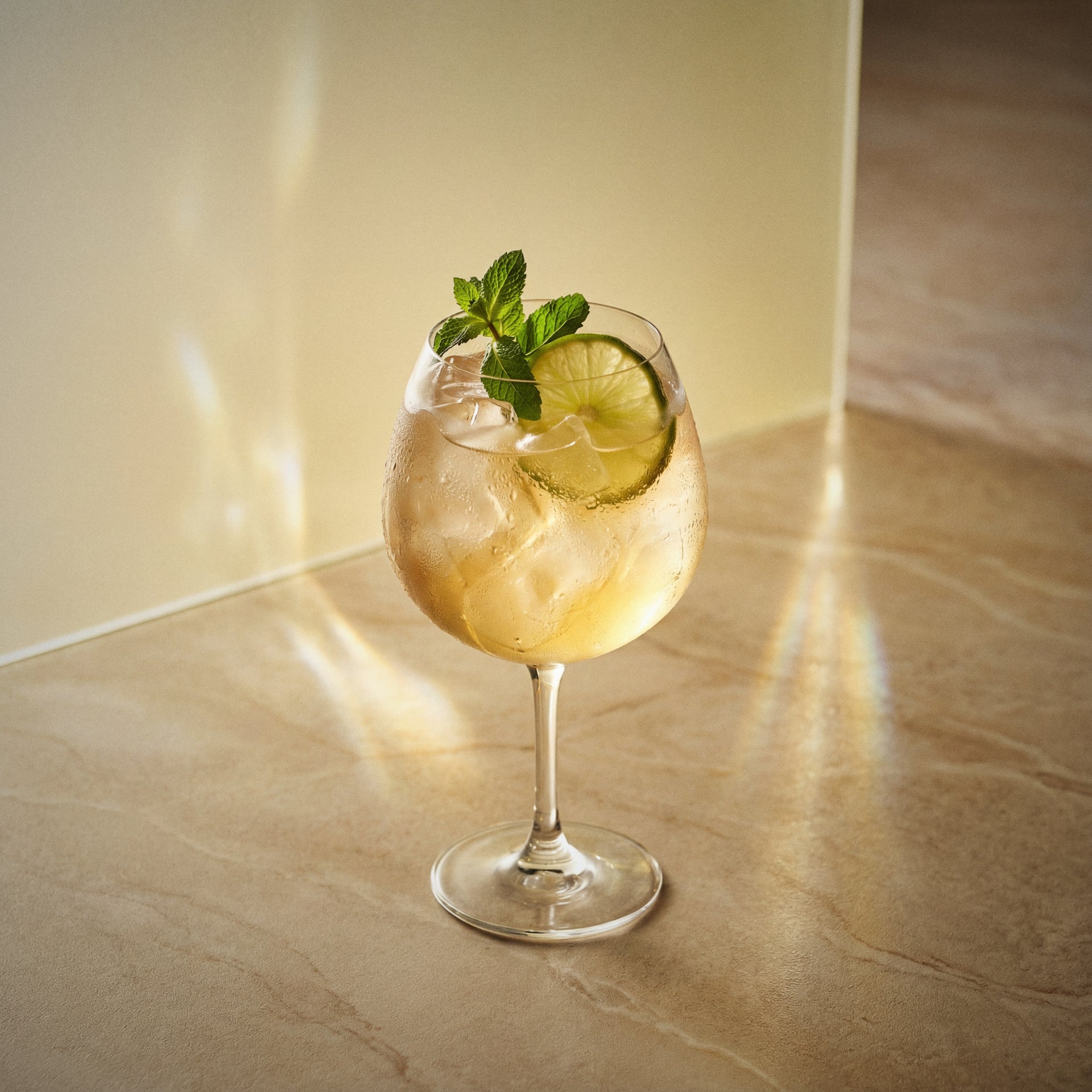 banana spritz cocktail with lime and mint in a coppa glass on a marble surface