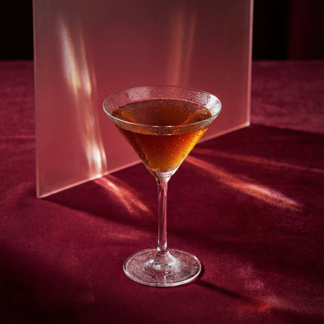 blood and sand cocktail with cherry brandy liqueur in a martini glass with a dark liquid on a red surface
