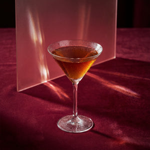 blood and sand cocktail with cherry brandy liqueur in a martini glass with a dark liquid on a red surface