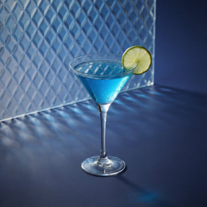 blue 1575 daiquiri cocktail with blue liqueur in a martini glass with a lime wheel on a dark surface.