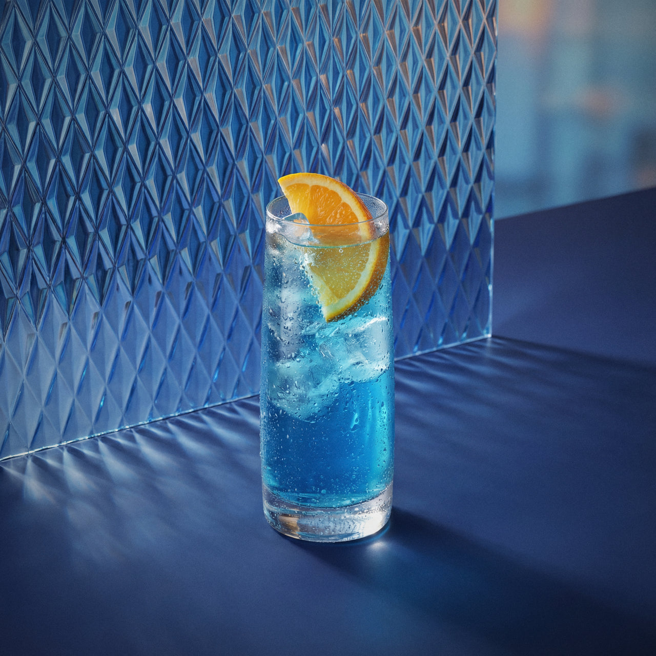 blue 1575 easy mix cocktail with blue liqueur in a highball glass with an orange wedge on a textured surface