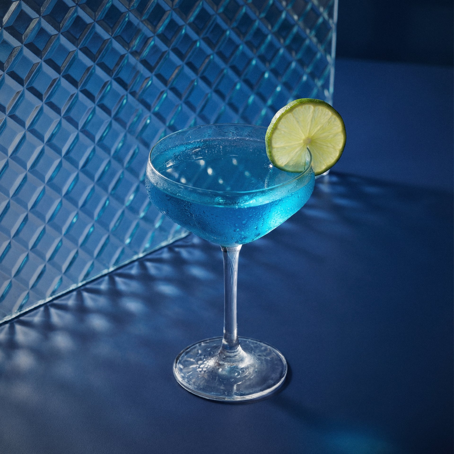 blue margarita with blue liqueur in a margarita glass with a lime wheel on a textured surface