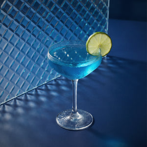 blue margarita with blue liqueur in a margarita glass with a lime wheel on a textured surface