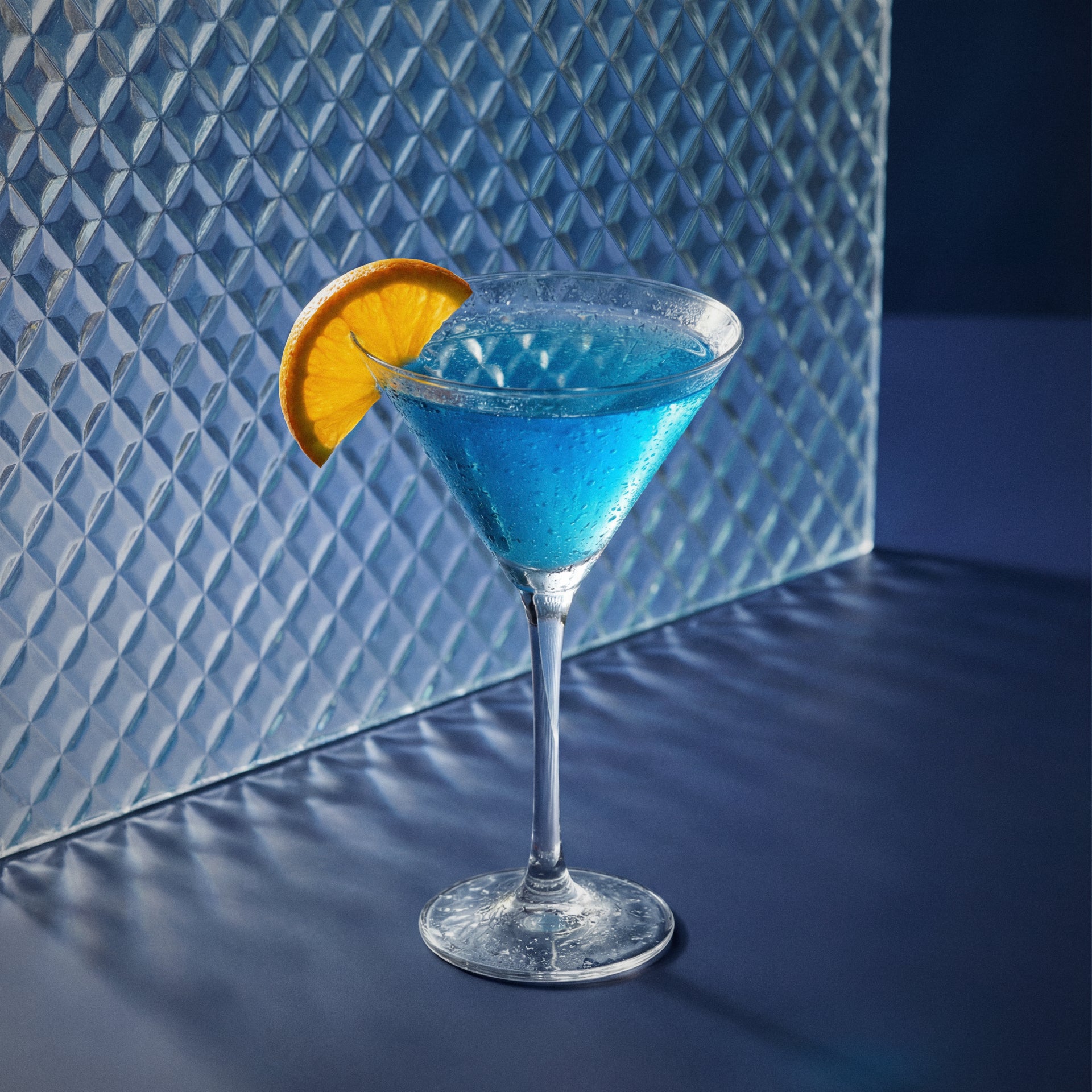 blue between the sheets cocktail with blue liqueur in a martini glass with an orange wedge on a textured surface