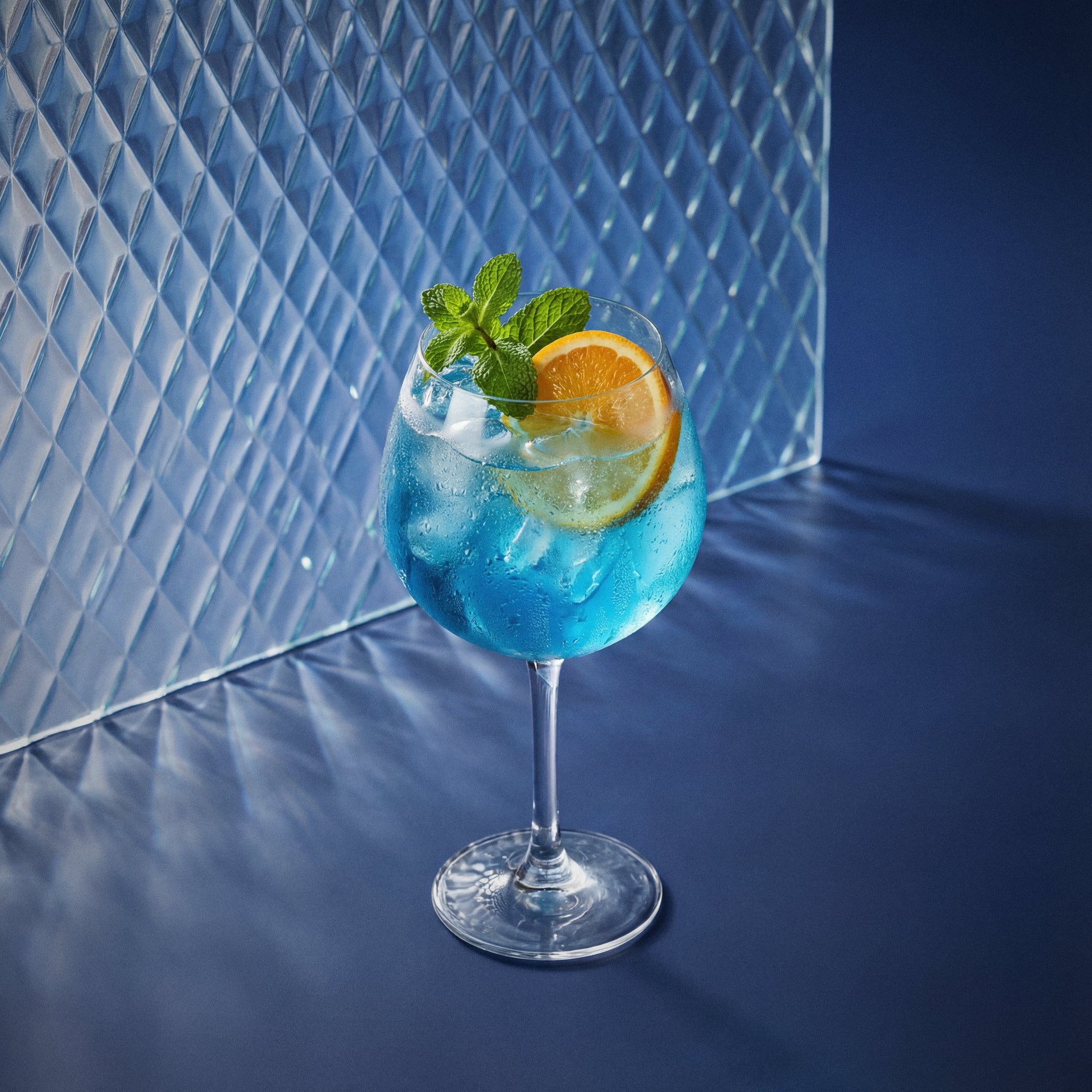 blue curacao spritz cocktail with blue curacao liqueur in a coppa glass with orange wheel and mint on a textured surface
