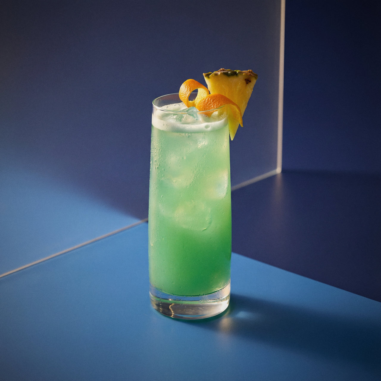 blue hawaii cocktail with blue curacao liqueur and vodka in a highball glass and with a pineapple wedge on a blue background