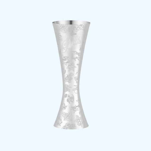 A silver metal jigger with an engraved floral and bird pattern and the brand name 'Bella' on the side, set against a solid light blue background.