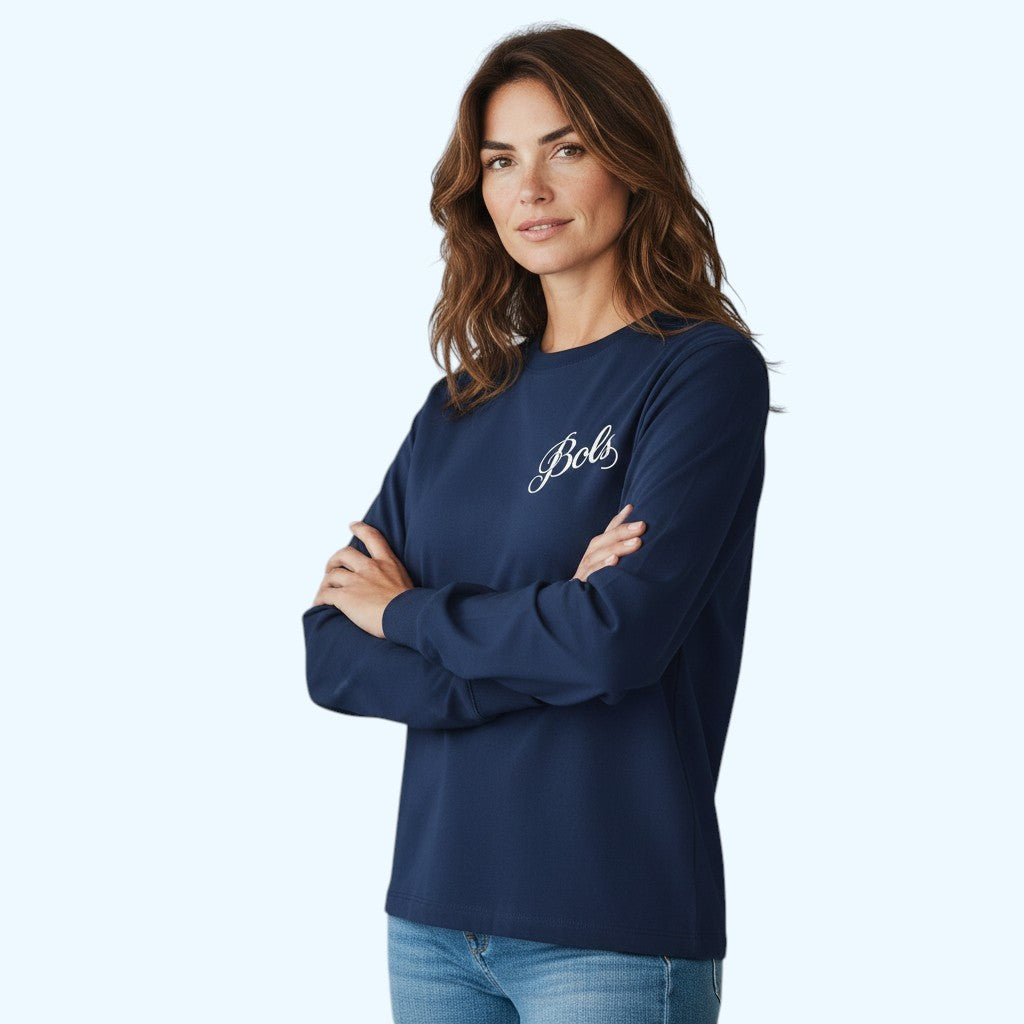 A woman modeling a navy blue long-sleeve crewneck shirt with 'Bols' embroidered in white script on the left chest, paired with blue jeans against a light blue studio background.