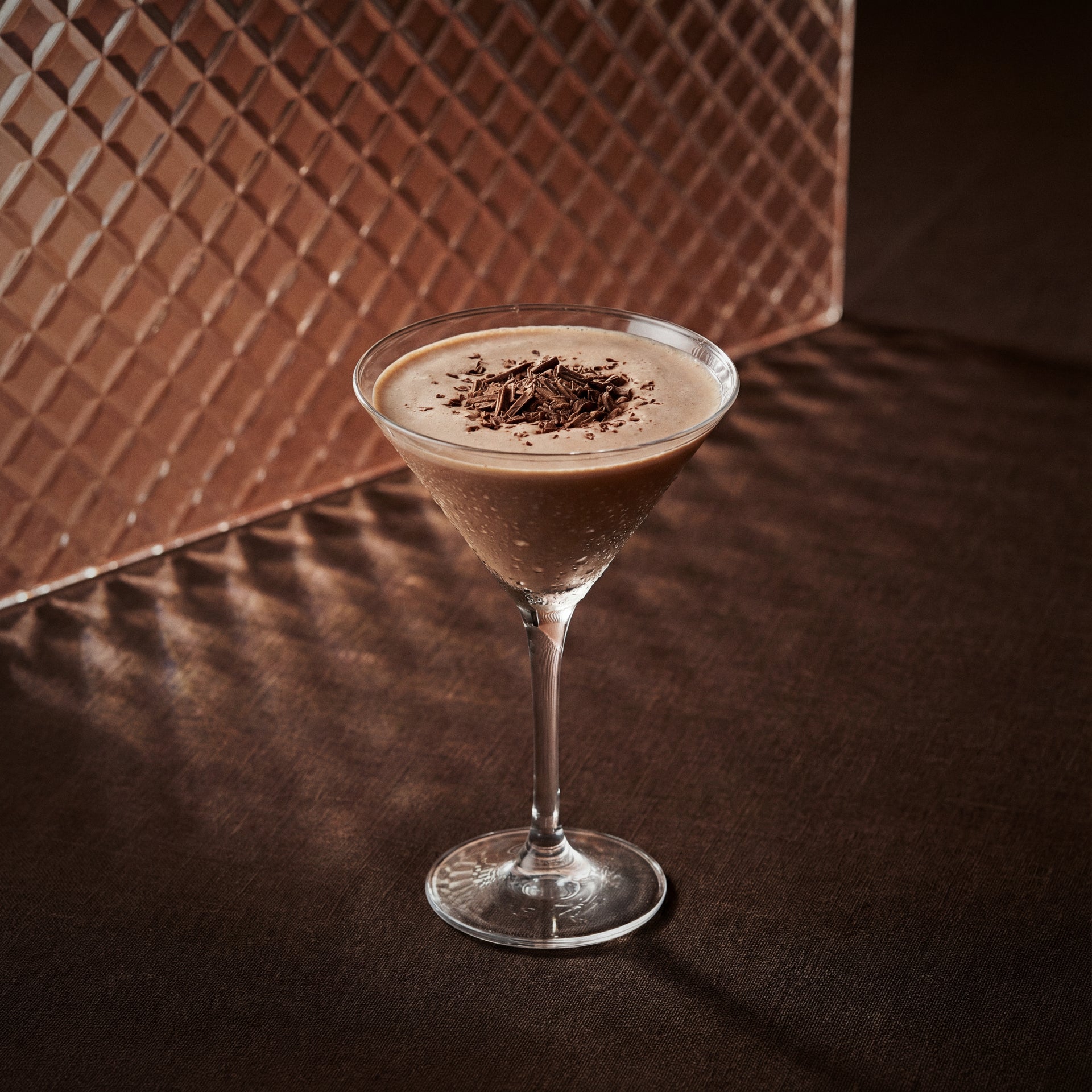 brandy alexander cocktail with cacao brown liqueur in a martini glass with chocolate flakes on a textured surface