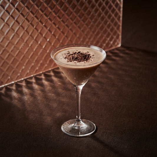 brandy alexander cocktail with cacao brown liqueur in a martini glass with chocolate flakes on a textured surface