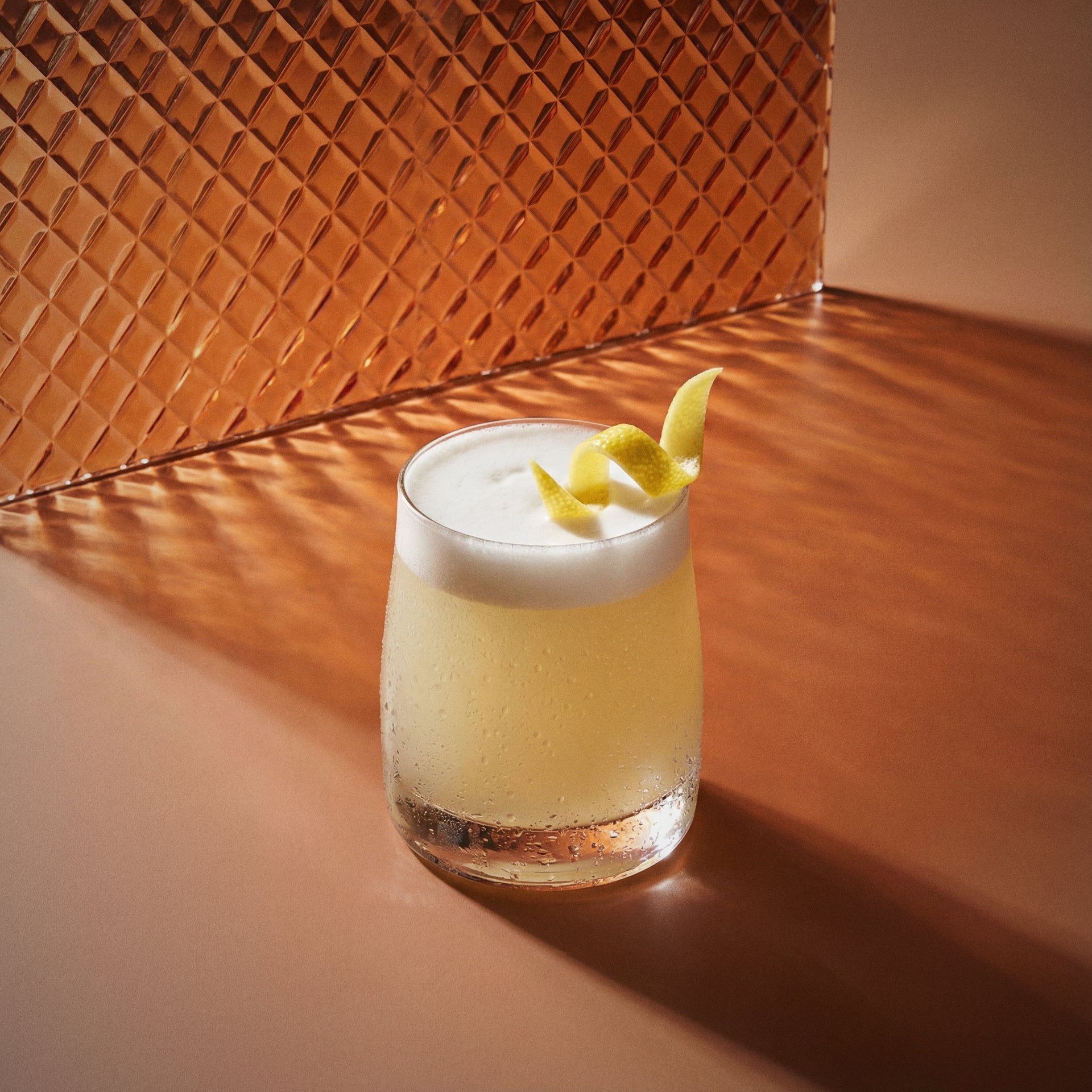 butterscotch sour cocktail with butterscotch liqueur and a lemon twist in a glass on a textured surface