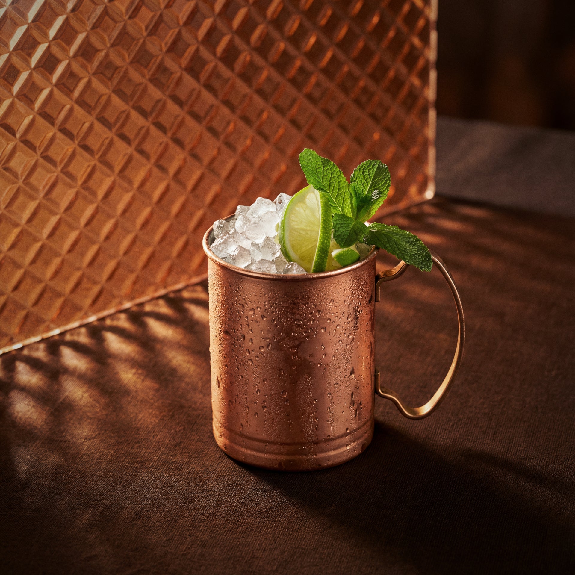 cacao brown mule cocktail in a copper mug with cacao brown liqueur and a lime wheel and mint sprig on a textured surface