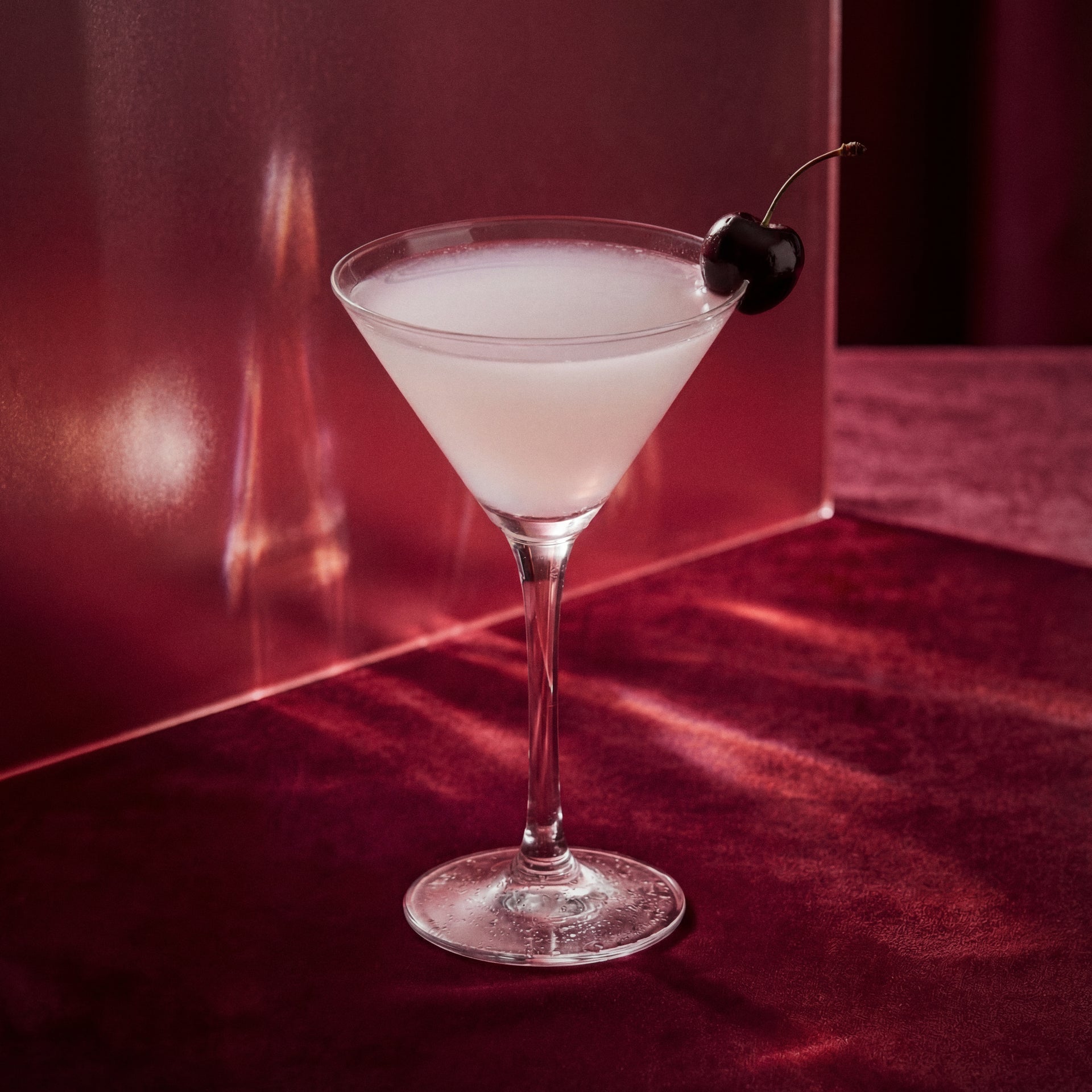cherry alexander cocktail with cherry brandy liqueur, cacao white liqueur, vodka, in a martini glass with a cherry on a red surface