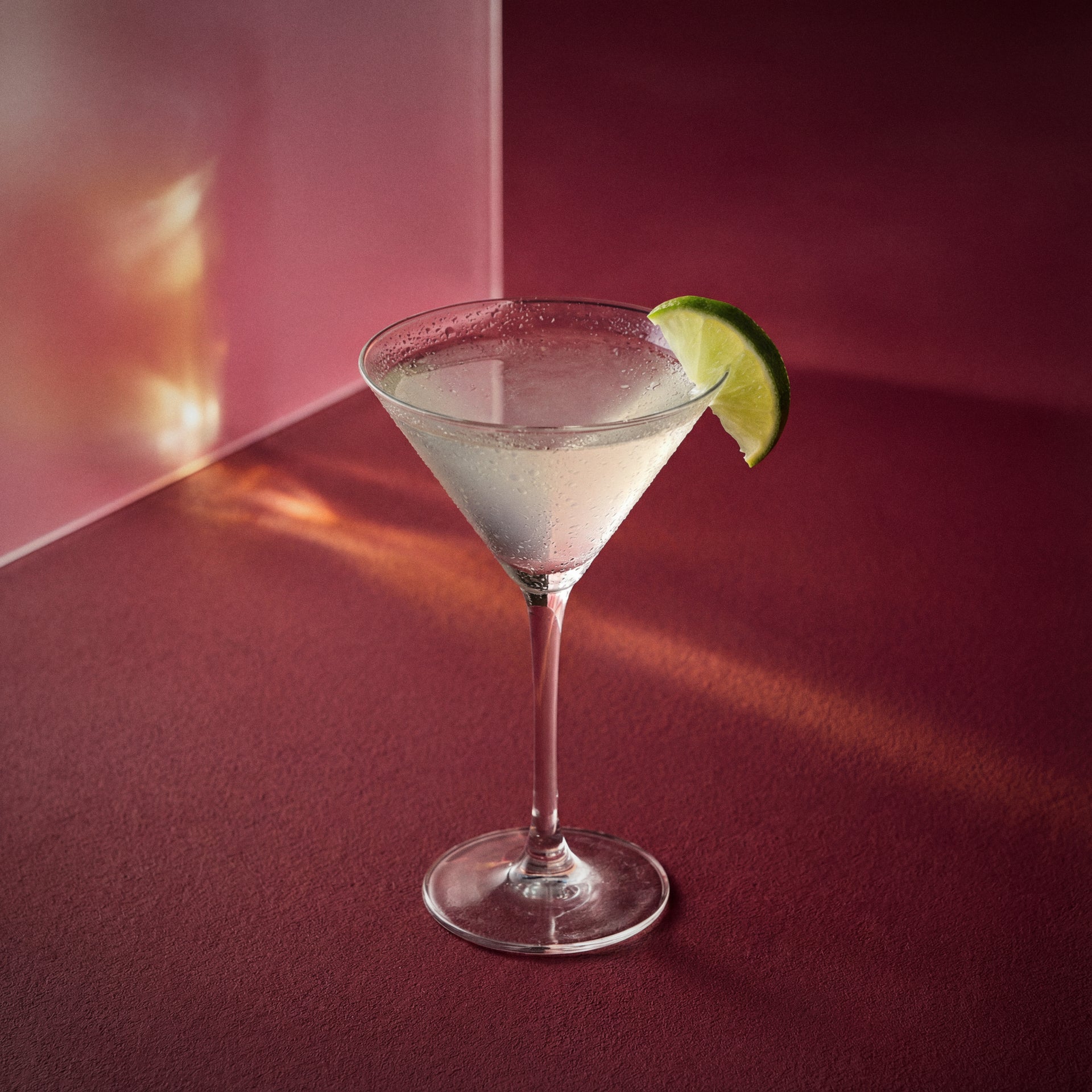 cherry daiquiri cocktail with kirsche liqueur in a martini glass with a lime wedge on a textured surface