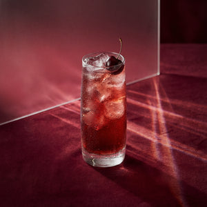 cherry easy mix cocktail with cherry brandy liqueur and a cherry in a highball glass on a textured surface