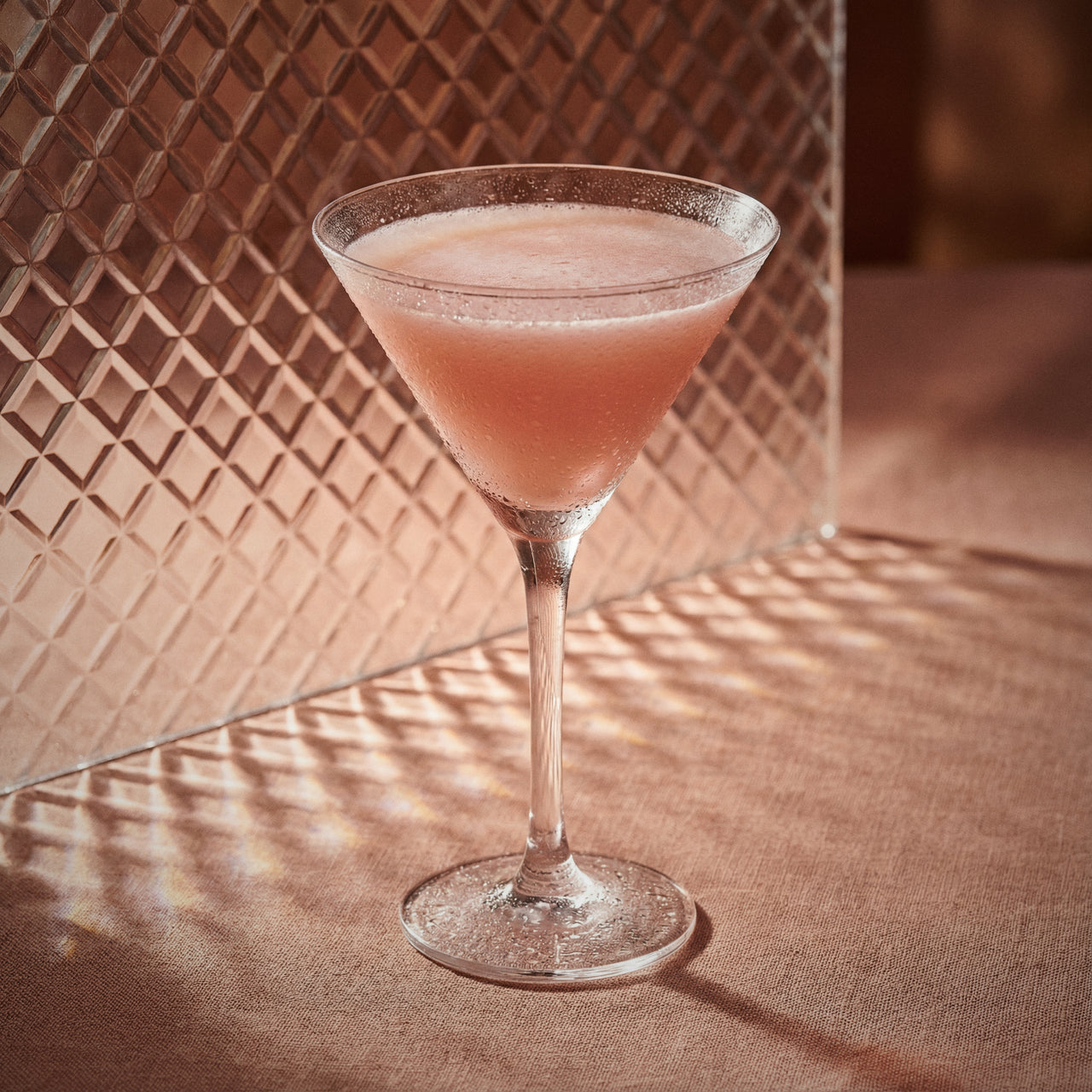 chocolate pumpkin cocktail in a martini glass with cacao white liqueur  on a textured surface with a patterned wall in the background