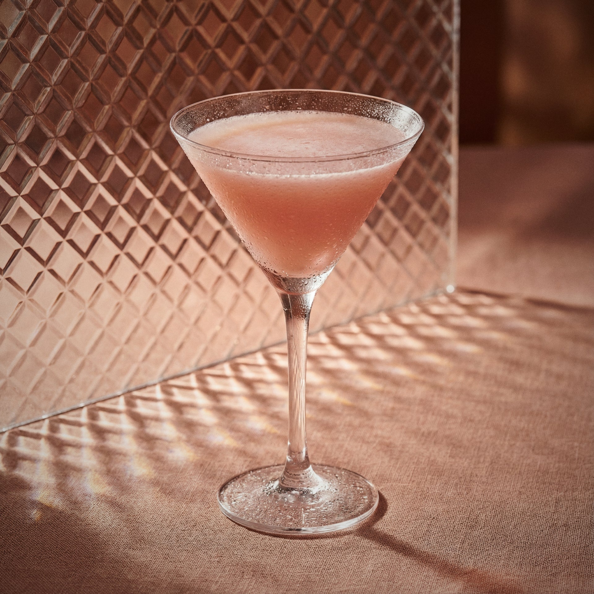 chocolate pumpkin cocktail in a martini glass with cacao white liqueur  on a textured surface with a patterned wall in the background