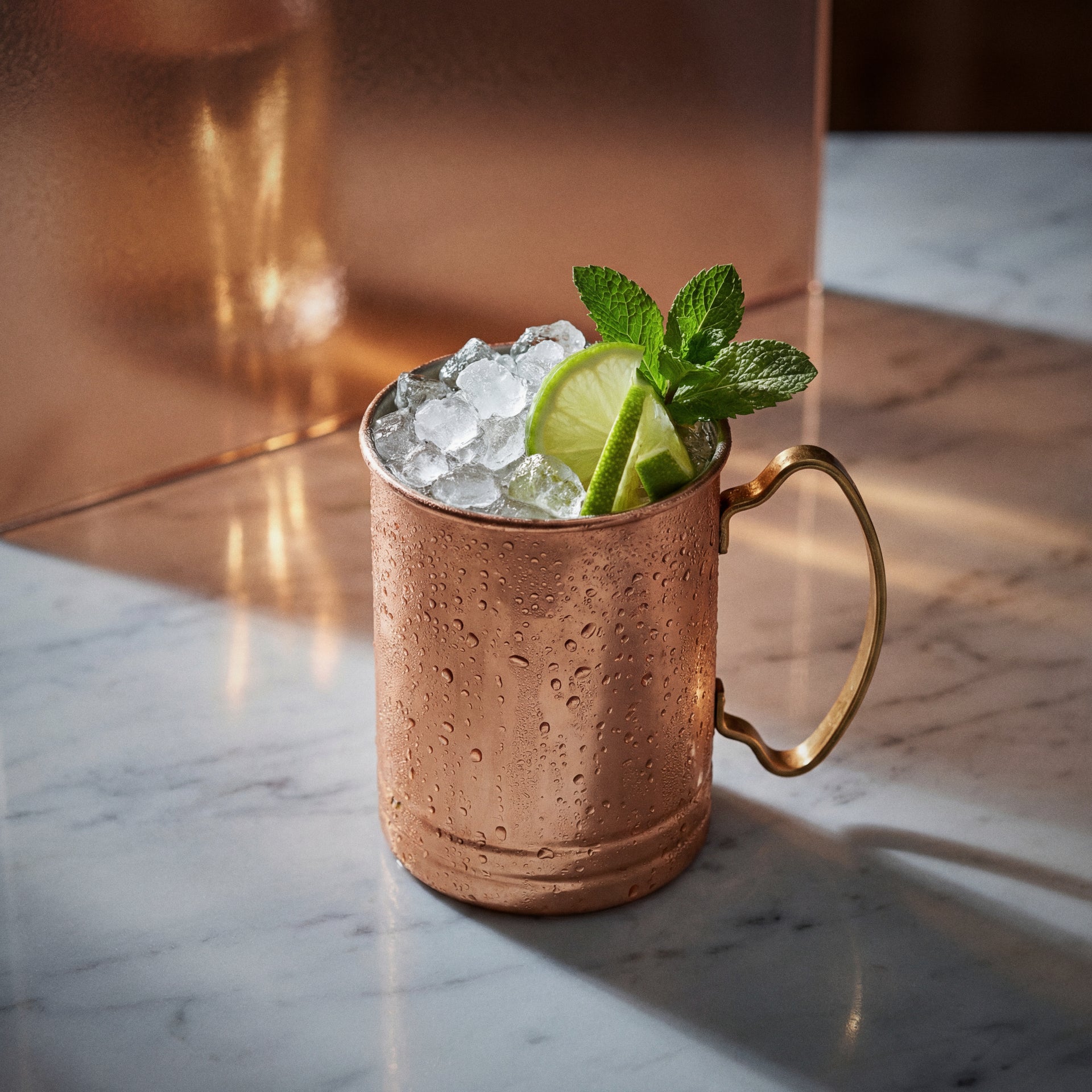 coconut mule cocktail with coconut liqueur in a copper mug with lime wheels and mint on a textured surface
