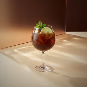 coffee spritz cocktail with coffee liqueur in a coppa glass with lime wheel and mint sprigs on a textured surface