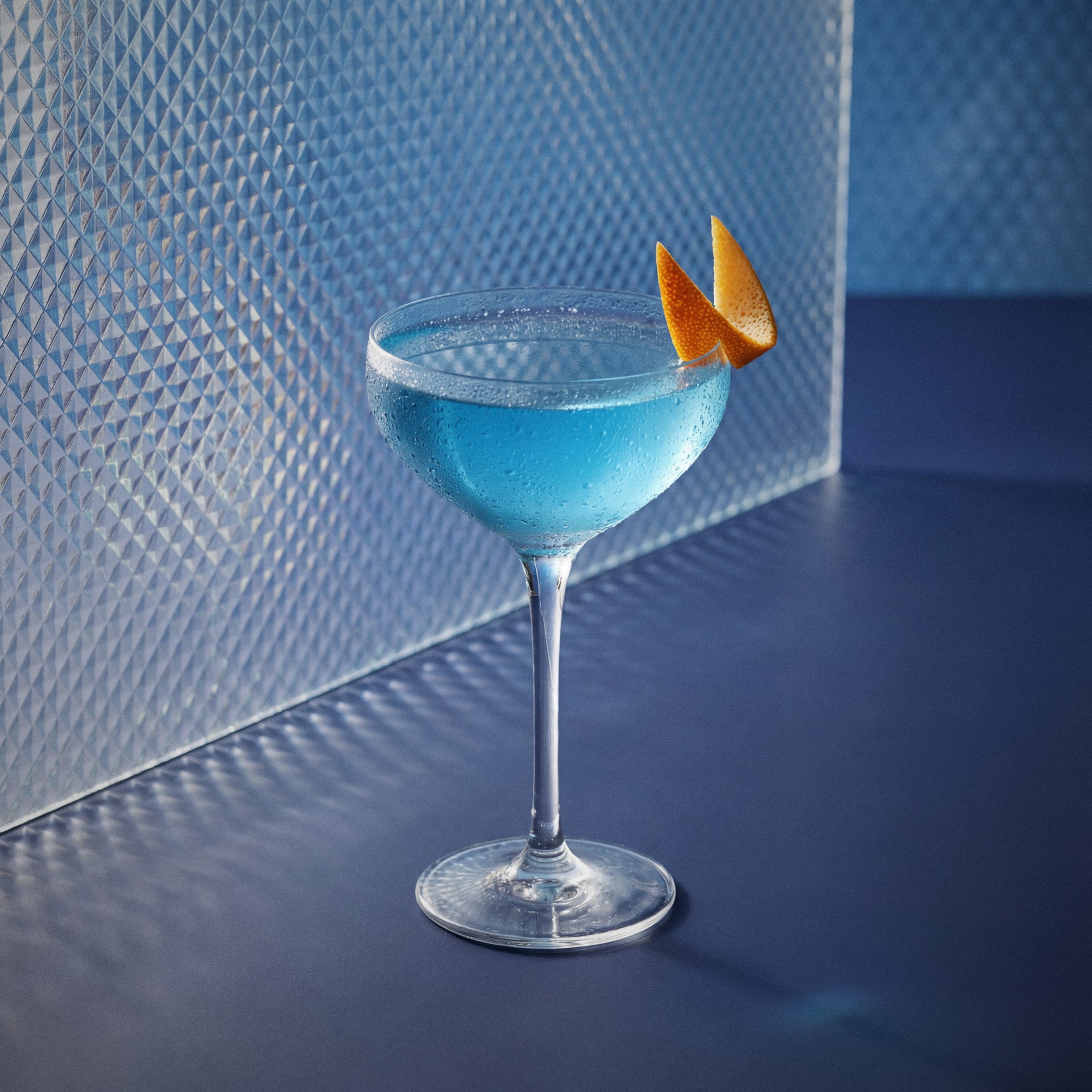 corpse reviver nr blue cocktail with bols blue 1575 liqueur and gin in a coupe glass with a orange garnish on a textured surface