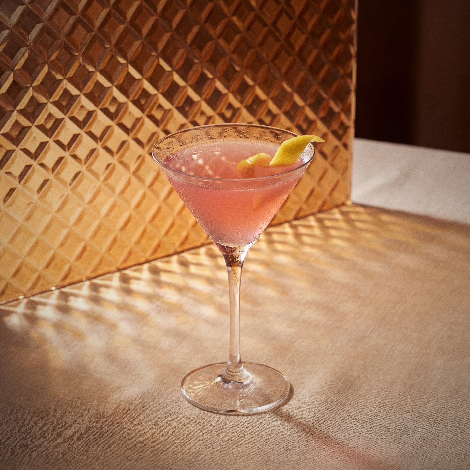 cosmopolitan cocktail with triple sec liqueur and vodka in a martini glass with a lemon twist on a textured surface.
