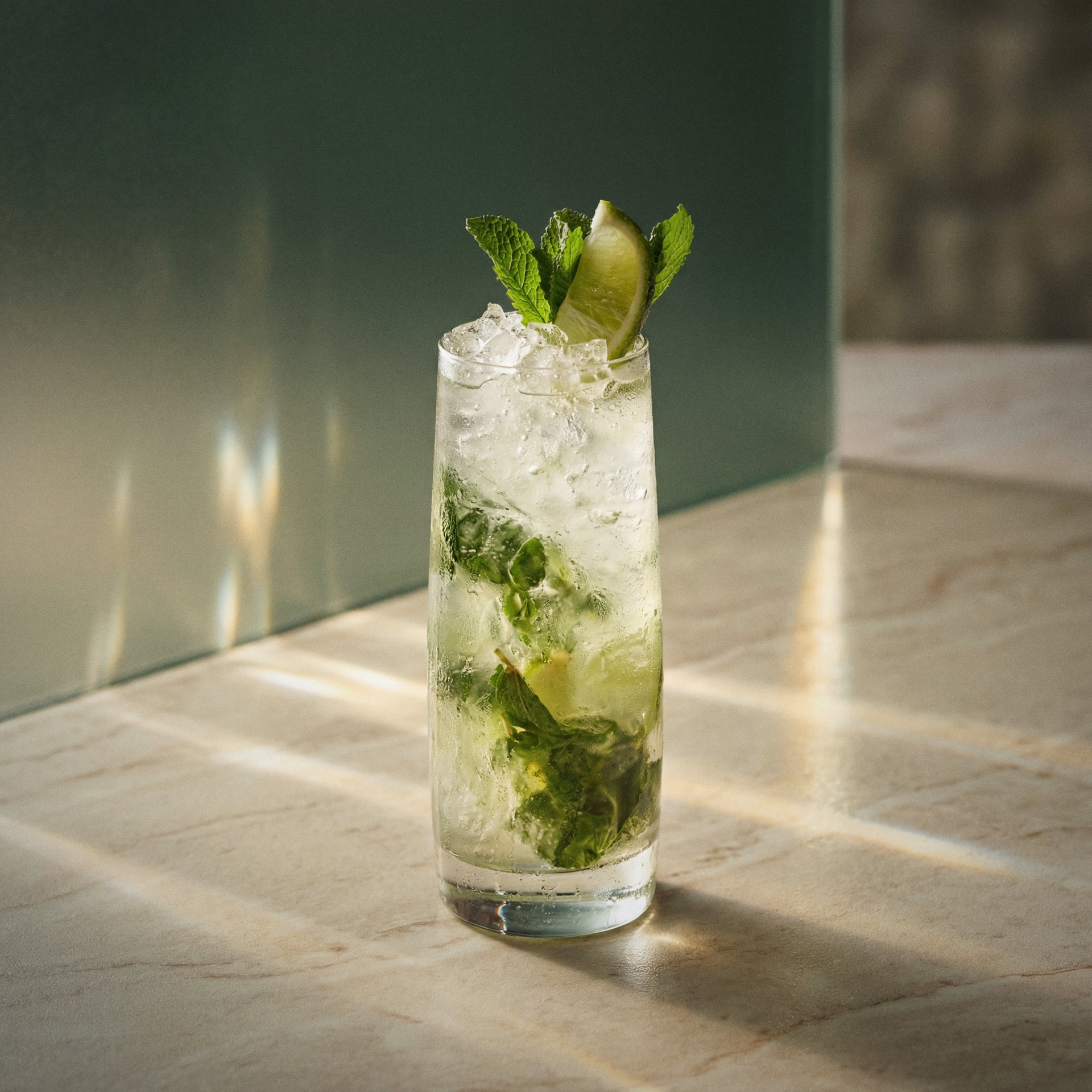 cucumber mojito cocktail with cucumber liqueur in a highball glass garnished with lime wedges and mint sprigs on a textured surface