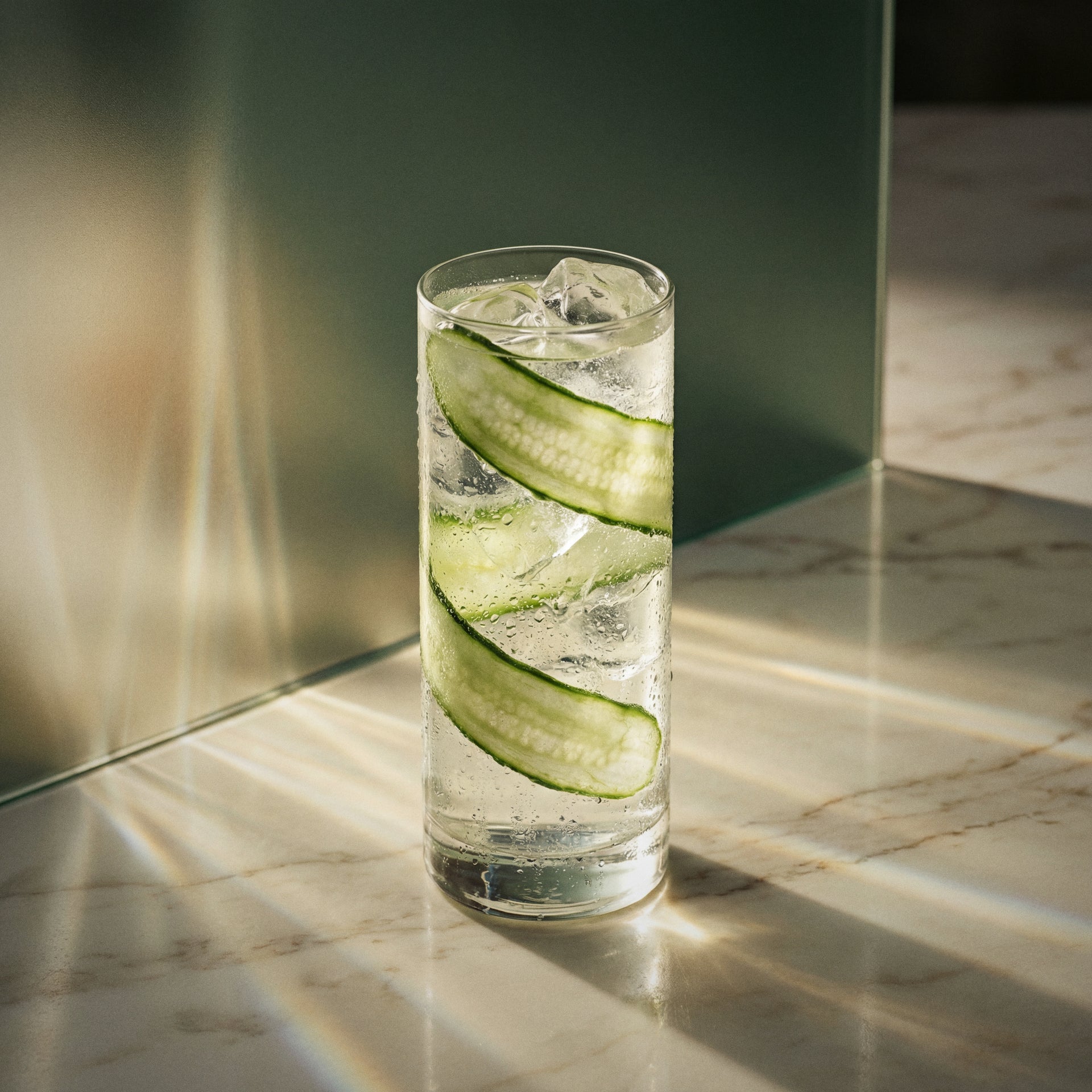 Glass of cucumber tonic cocktail with cucumber liqueur in a highball glass with cucumber as garnish on a marble surface