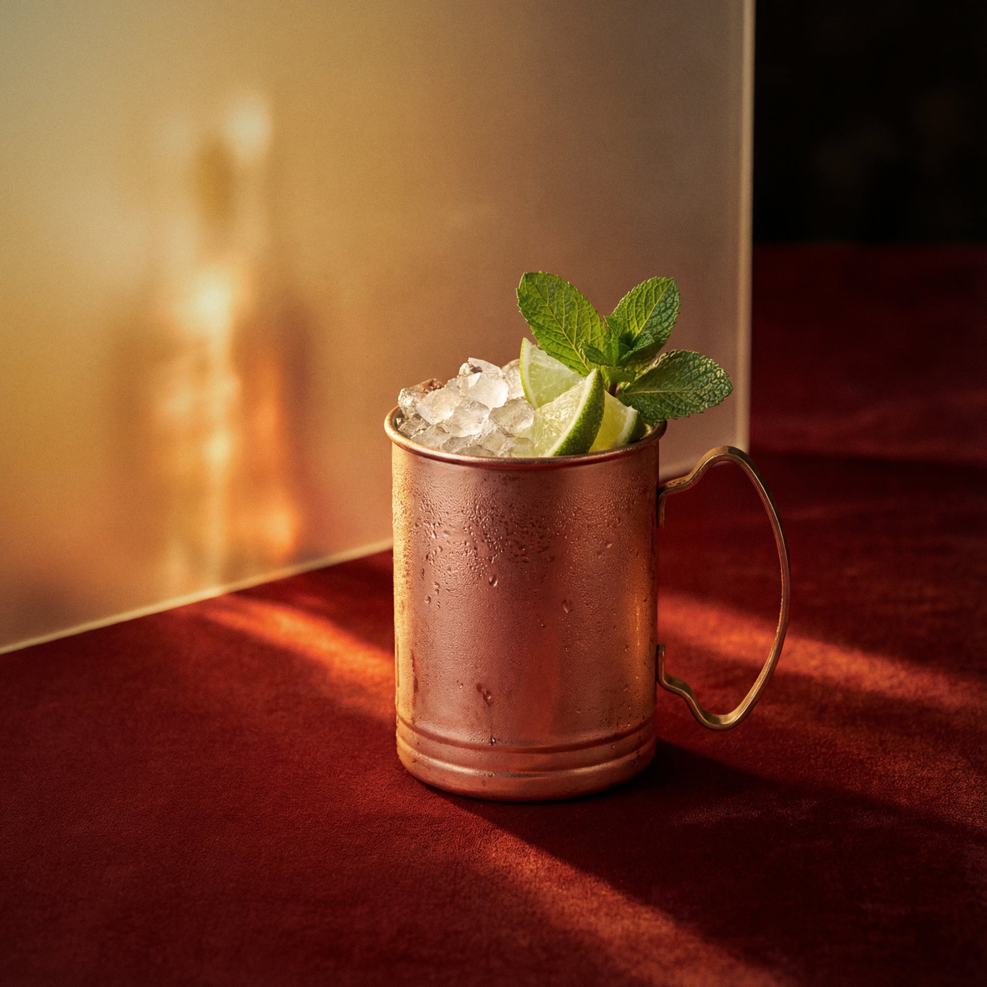 dry orange mule cocktail with dry orange liqueur in a copper mug garnished with lime and mint leaves on a red surface