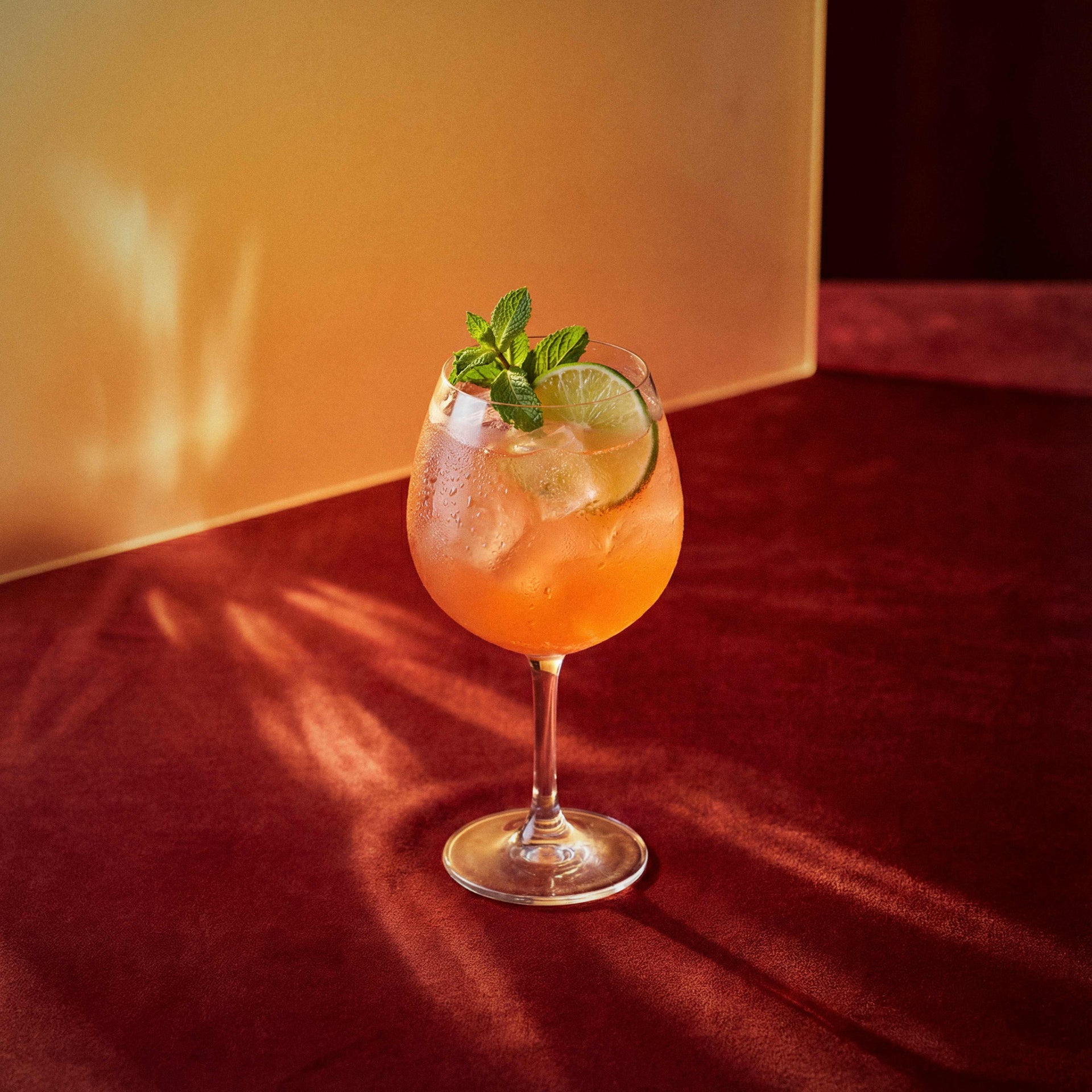 dry orange spritz cocktail with dry orange liqueur in a coppa glass with a lime wheel and mint sprig on a textured surface