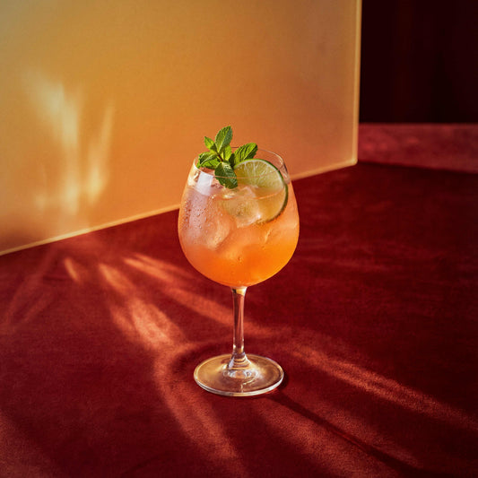 dry orange spritz cocktail with dry orange liqueur in a coppa glass with a lime wheel and mint sprig on a textured surface