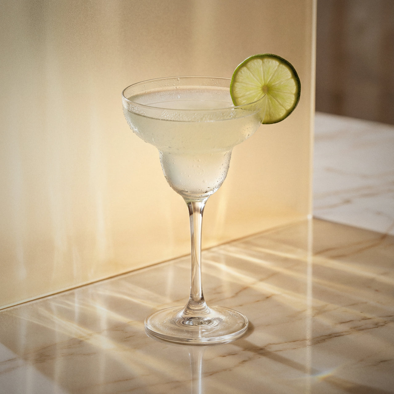 elderflower margarita cocktail with elderflower liqueur in a margarita glass with a lime wheel on a textured surface