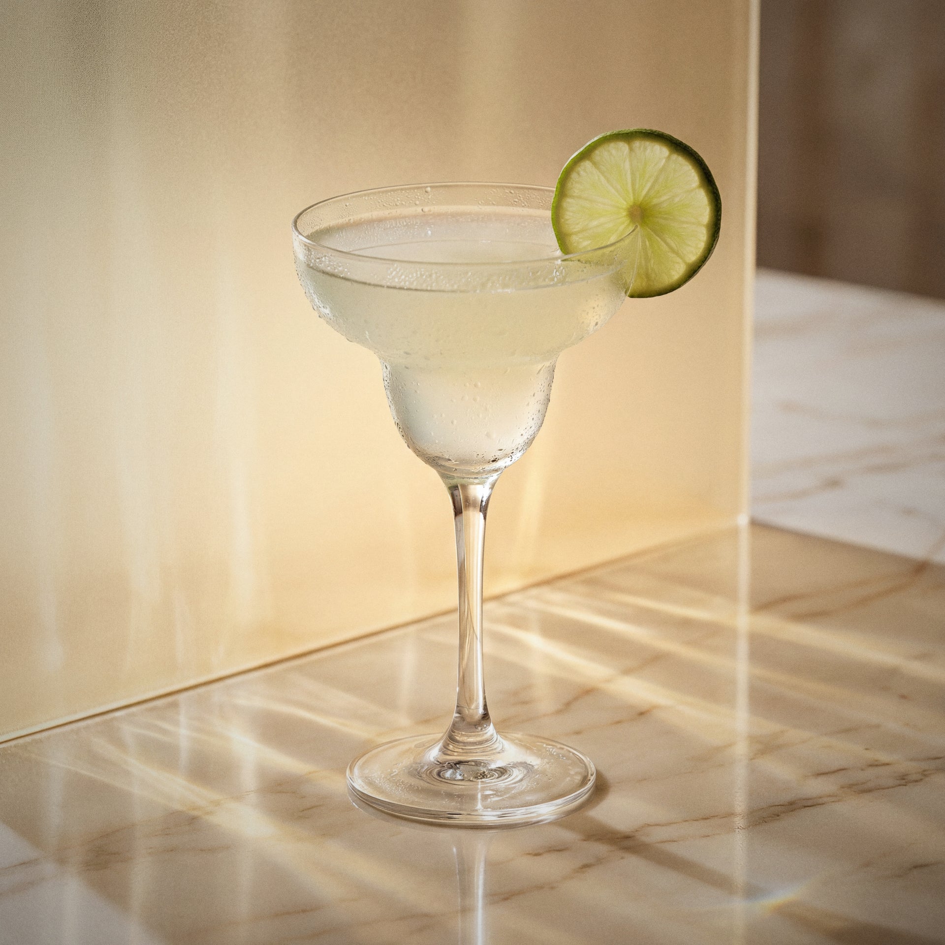 elderflower margarita cocktail with elderflower liqueur in a margarita glass with a lime wheel on a textured surface