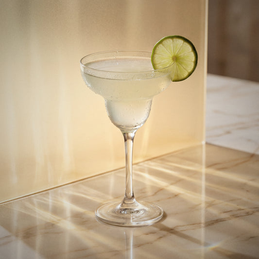 elderflower margarita cocktail with elderflower liqueur in a margarita glass with a lime wheel on a textured surface