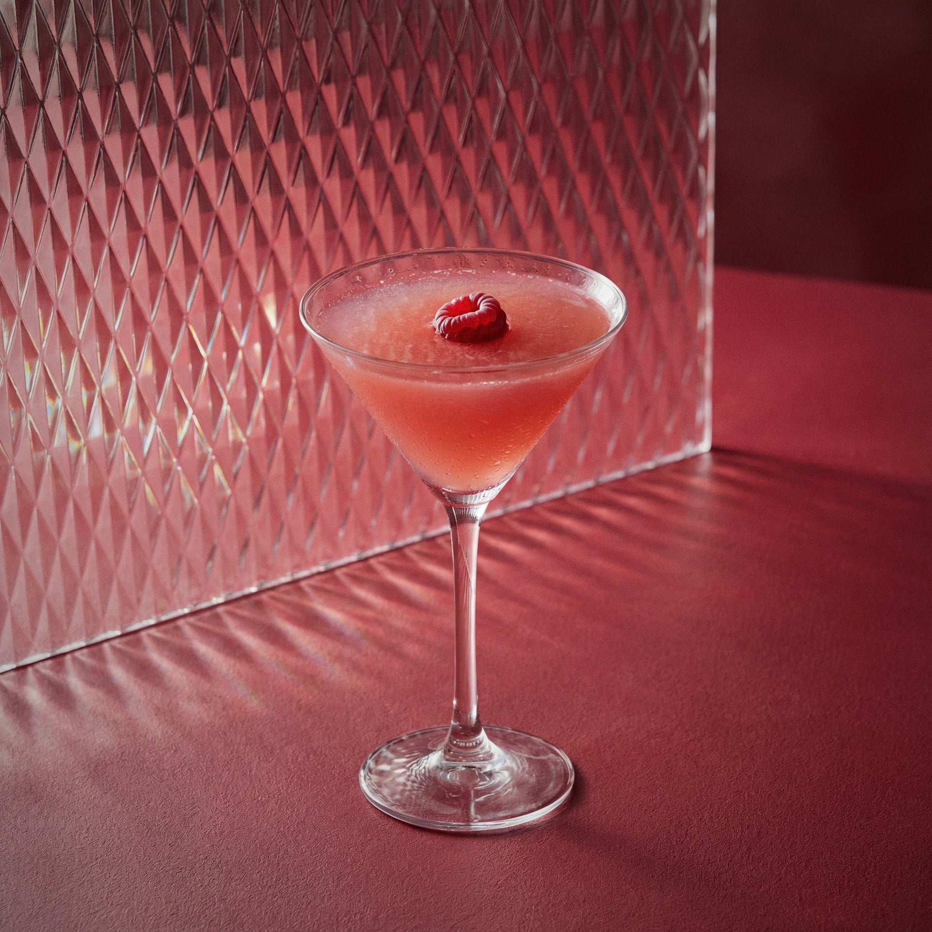 french martini cocktail with a raspberry and raspberry liqueur in a martini glass on a red surface with a textured red wall background.