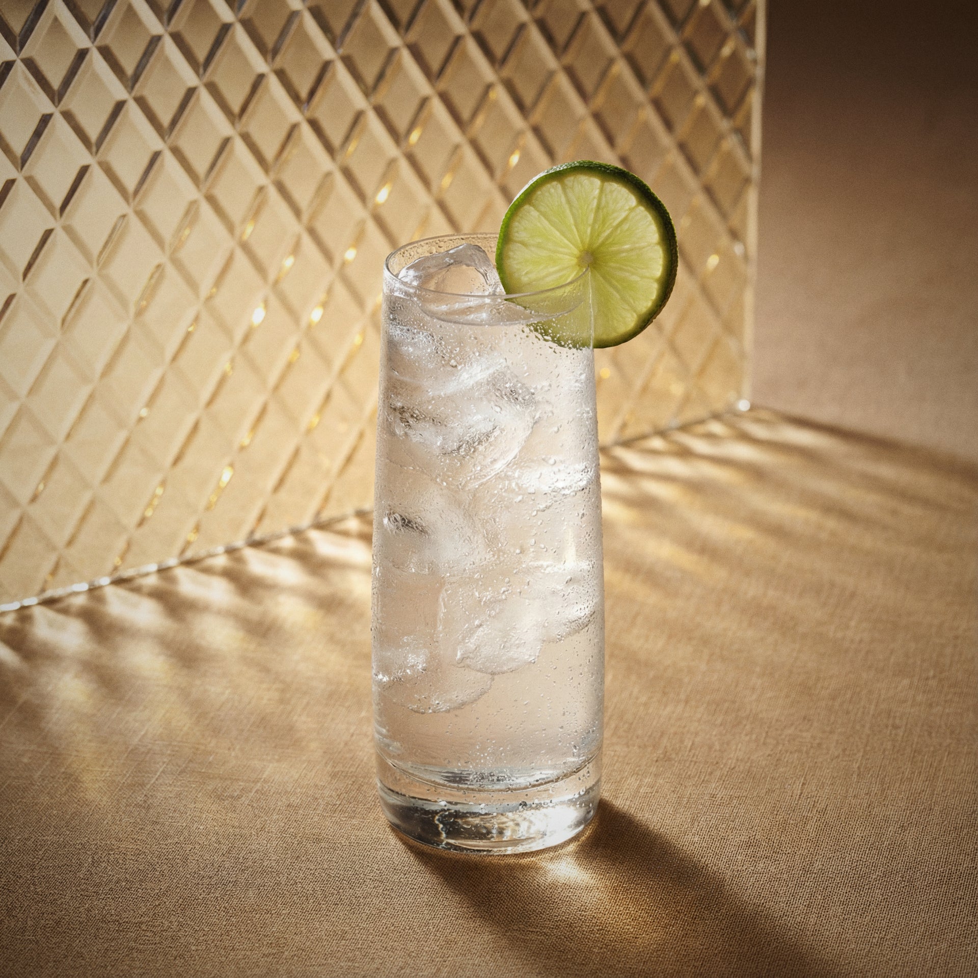 ginger easy mix cocktail in aighball glass with a lime wedge with ginger liqueur on a textured surfaceh