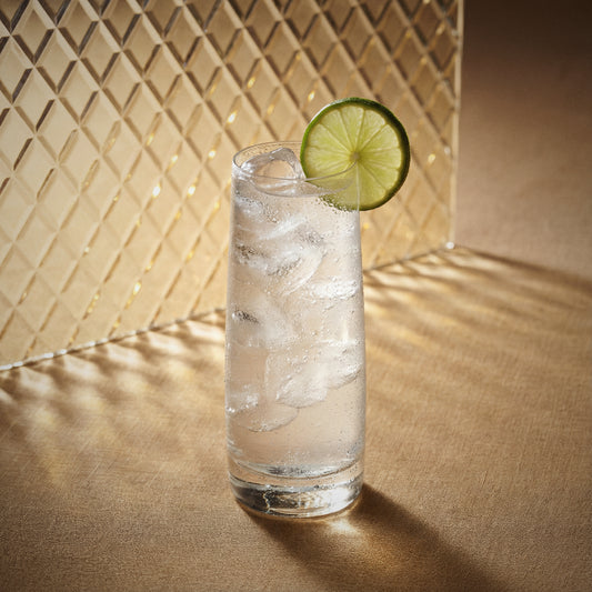 ginger easy mix cocktail in aighball glass with a lime wedge with ginger liqueur on a textured surfaceh