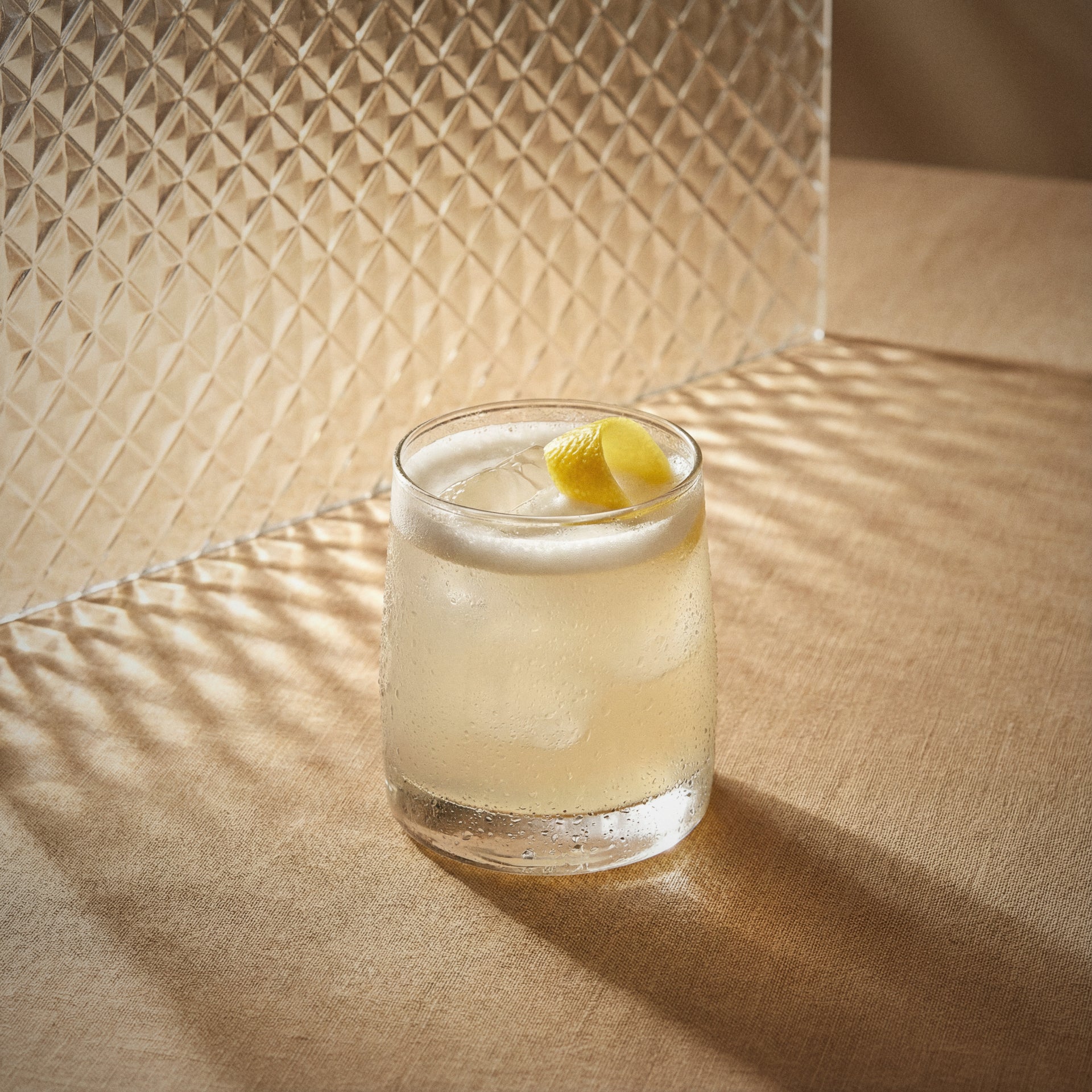 ginger sour cocktail in a rocks glass with a lemon twist with ginger liqueur on a textured surface with sunlight casting shadows