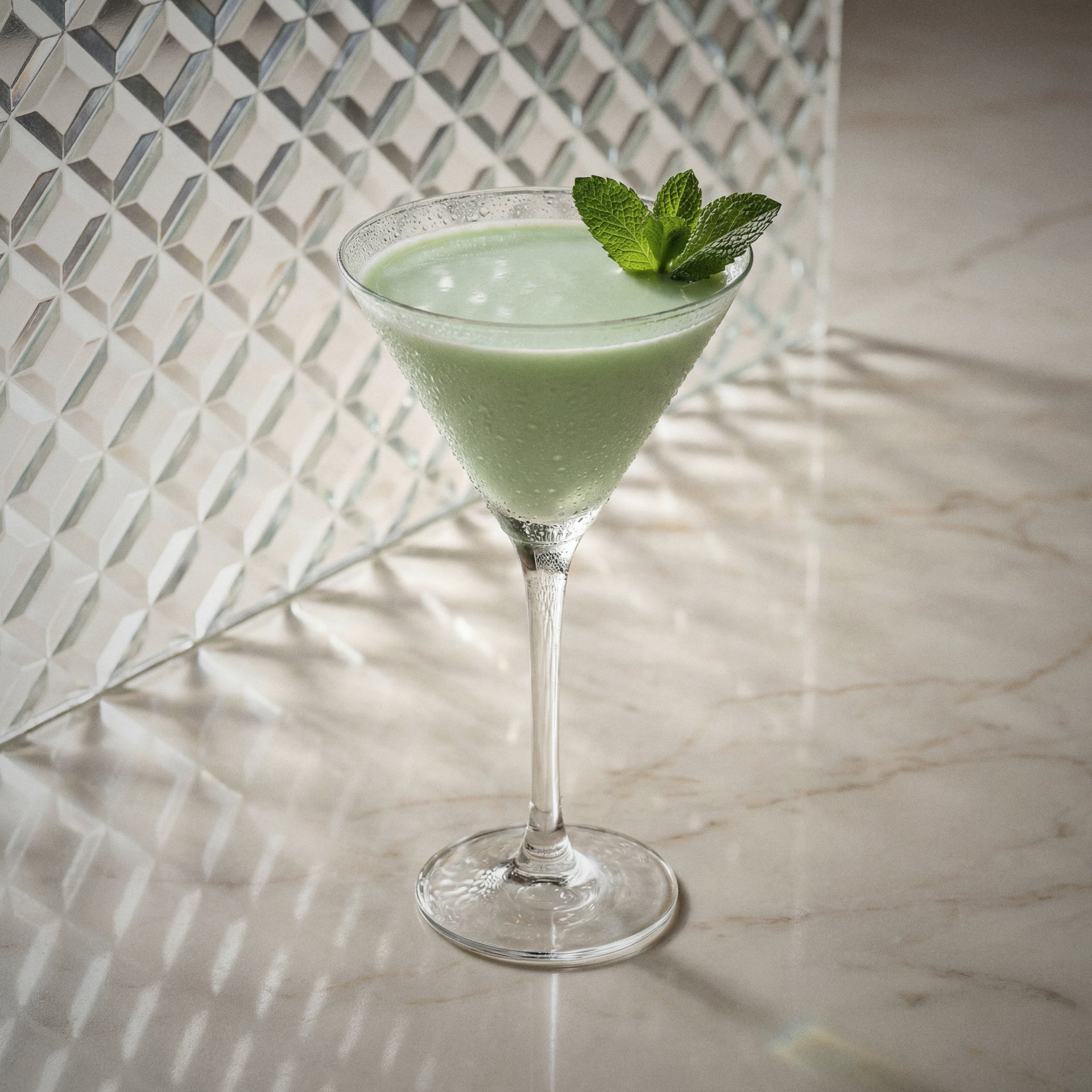 grasshopper cocktail in a martini glass with mint garnish made with natural yoghurt liqueur, peppermint green liqueur, and cacao white liqueur, on a textured surface