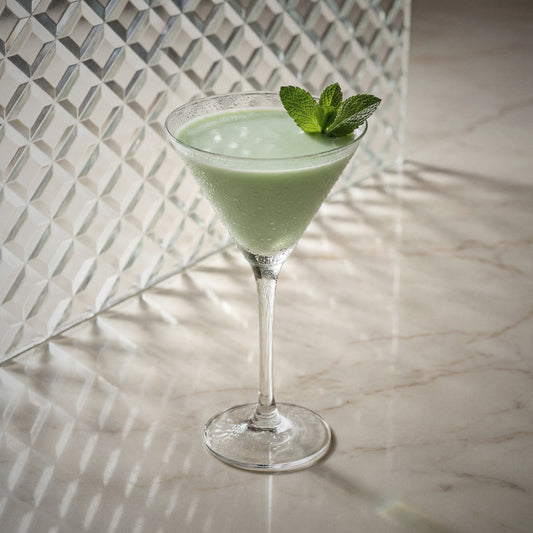 grasshopper cocktail in a martini glass with mint garnish made with natural yoghurt liqueur, peppermint green liqueur, and cacao white liqueur, on a textured surface