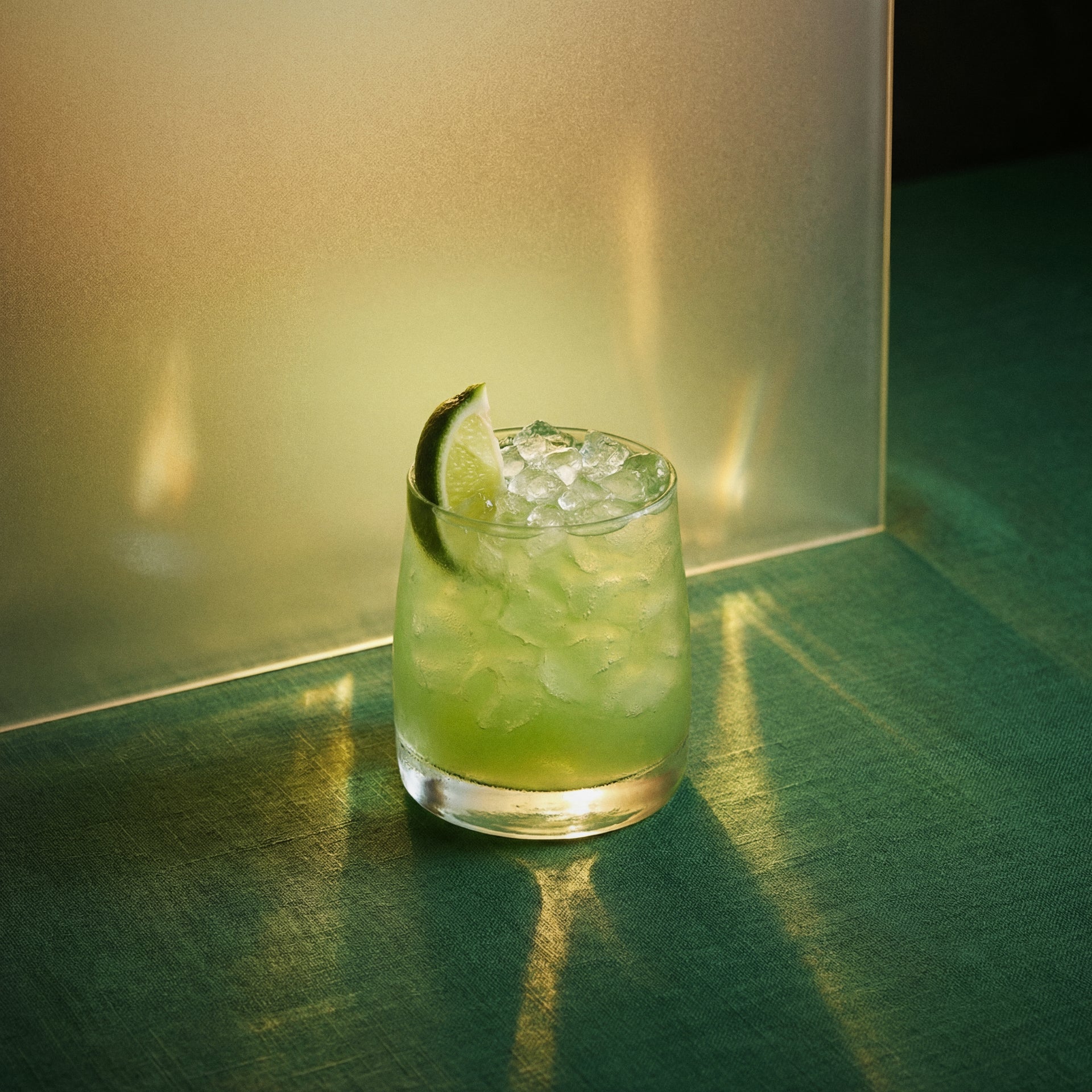 Green banana caipiroshka cocktail with green banana liqueur and vodka and with a lime wedge in a rocks glass on a reflective surface